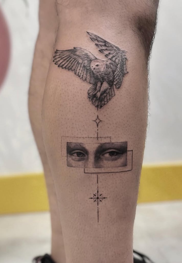 A black and grey illustrative tattoo on the calf featuring a detailed owl in flight above a geometric design with a pair of eyes and a star-like symbol — by Jian Liang, los angeles