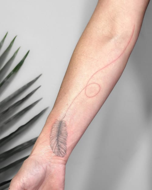 A delicate fine line feather tattoo on the forearm with a minimalist design and subtle black and grey shading — by Melanie Benoit, los angeles