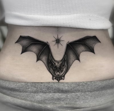 A black and grey realism tattoo of a bat with outstretched wings on the stomach, featuring detailed shading and a star above it — by Jian Liang, los angeles