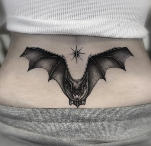 A black and grey realism tattoo of a bat with outstretched wings on the stomach, featuring detailed shading and a star above it — by Jian Liang, los angeles