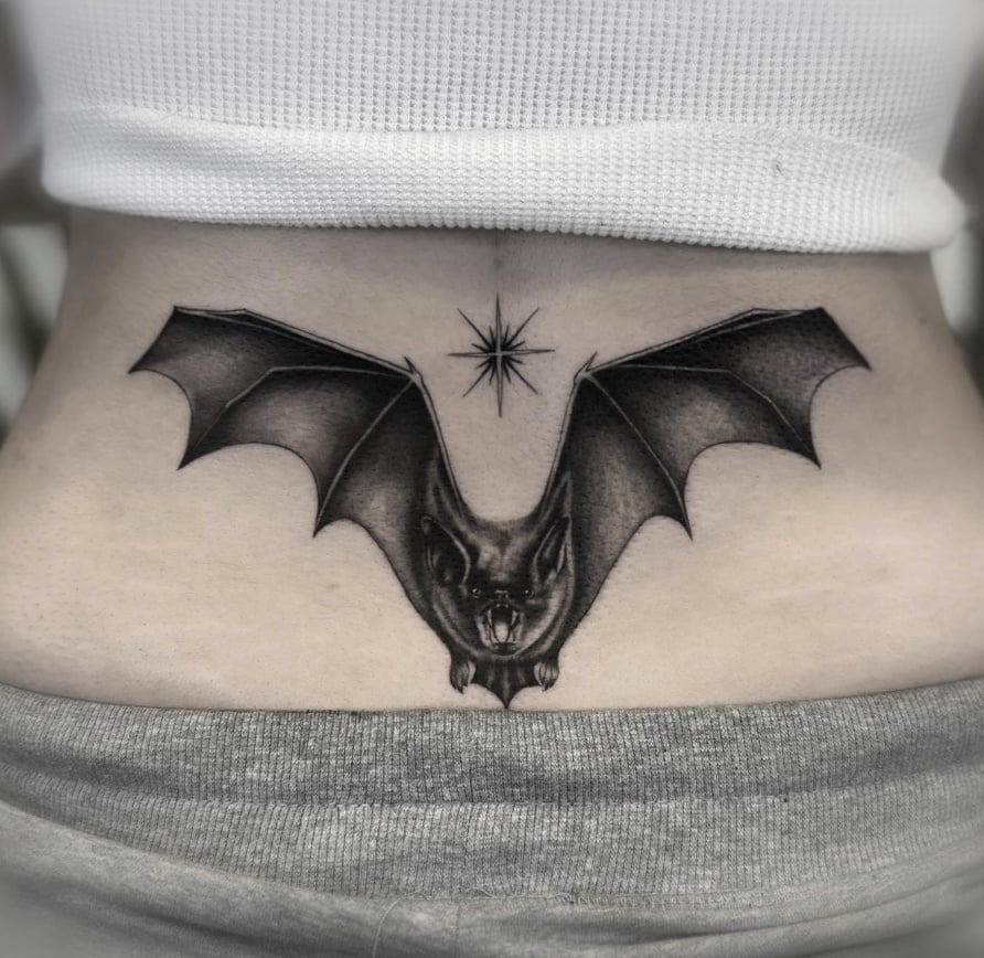 A black and grey realism tattoo of a bat with outstretched wings on the stomach, featuring detailed shading and a star above it — by Jian Liang, los angeles