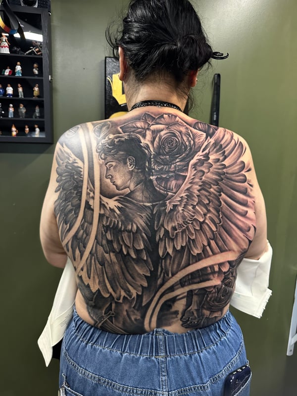A detailed black and grey tattoo of an angel with wings and roses covering the full back — by Humilde tattoos, los angeles