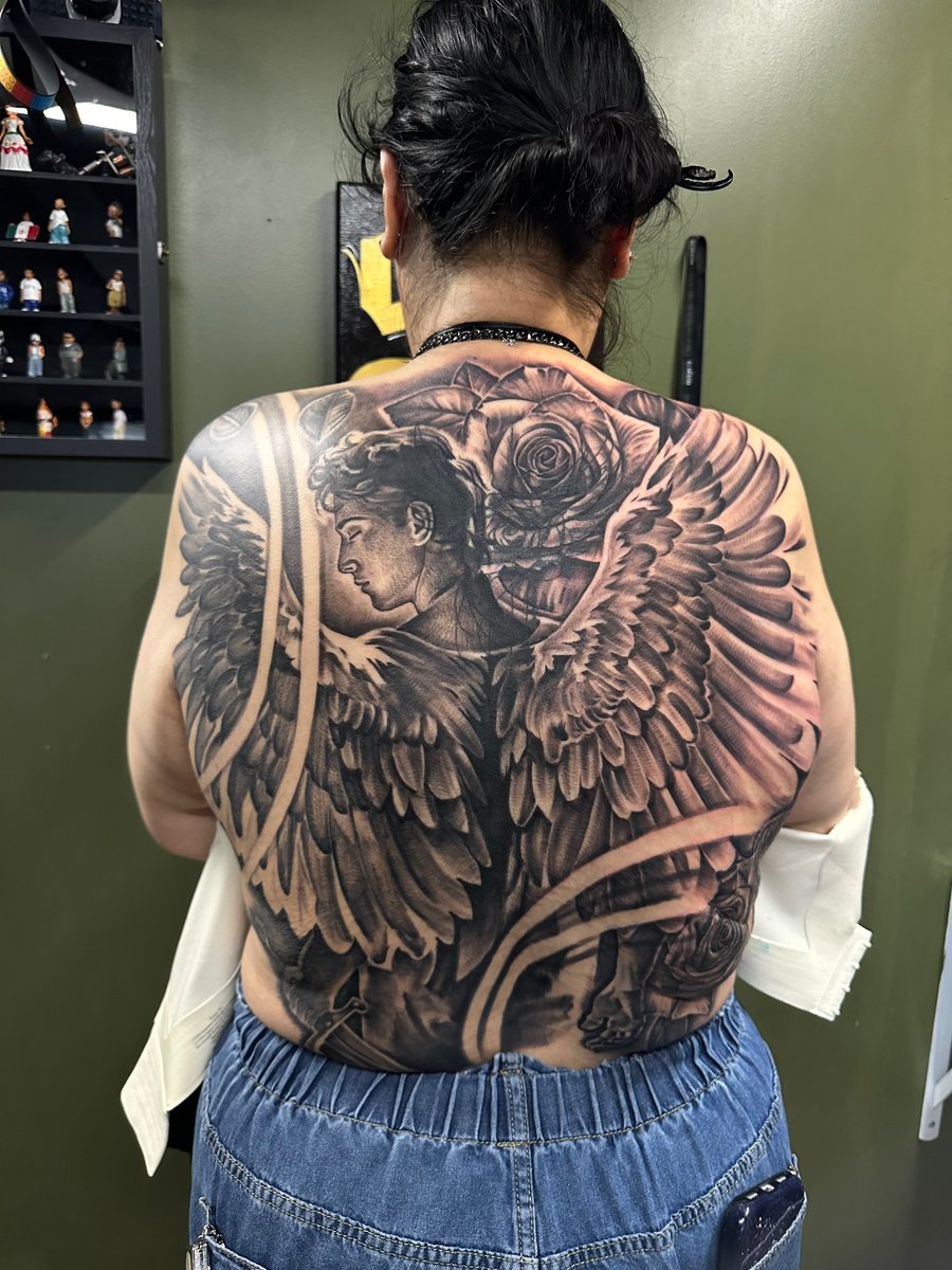 A detailed black and grey tattoo of an angel with wings and roses covering the full back — by Humilde tattoos, los angeles
