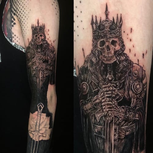 A detailed black and grey tattoo of a skeleton king holding a sword on the arm, featuring ornate armor and a crown — by Sandra Price, los angeles