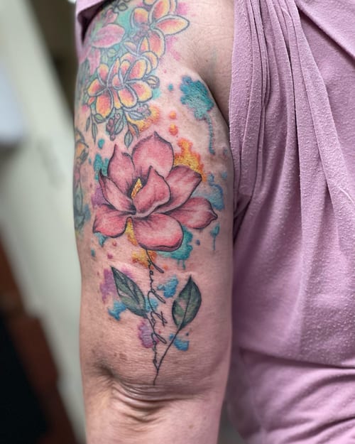 A colorful watercolor flower tattoo on the upper arm with delicate and whimsical floral elements — by Sandra Price, los angeles