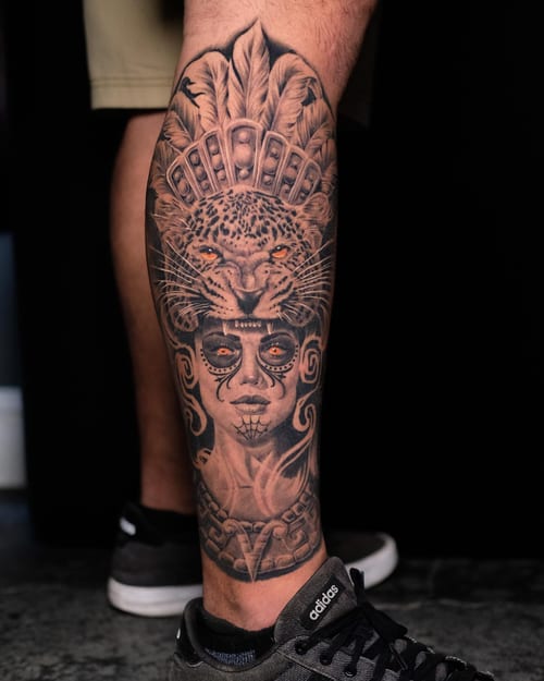 A bold black and grey tattoo of a woman with a jaguar headdress on the leg, featuring intricate details and ornate design — by Johnny Ayala, los angeles
