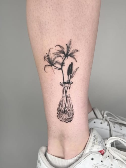 A fine line blackwork tattoo of flowers in a vase on the calf, featuring delicate lines and shading — by Level tattoo, los angeles