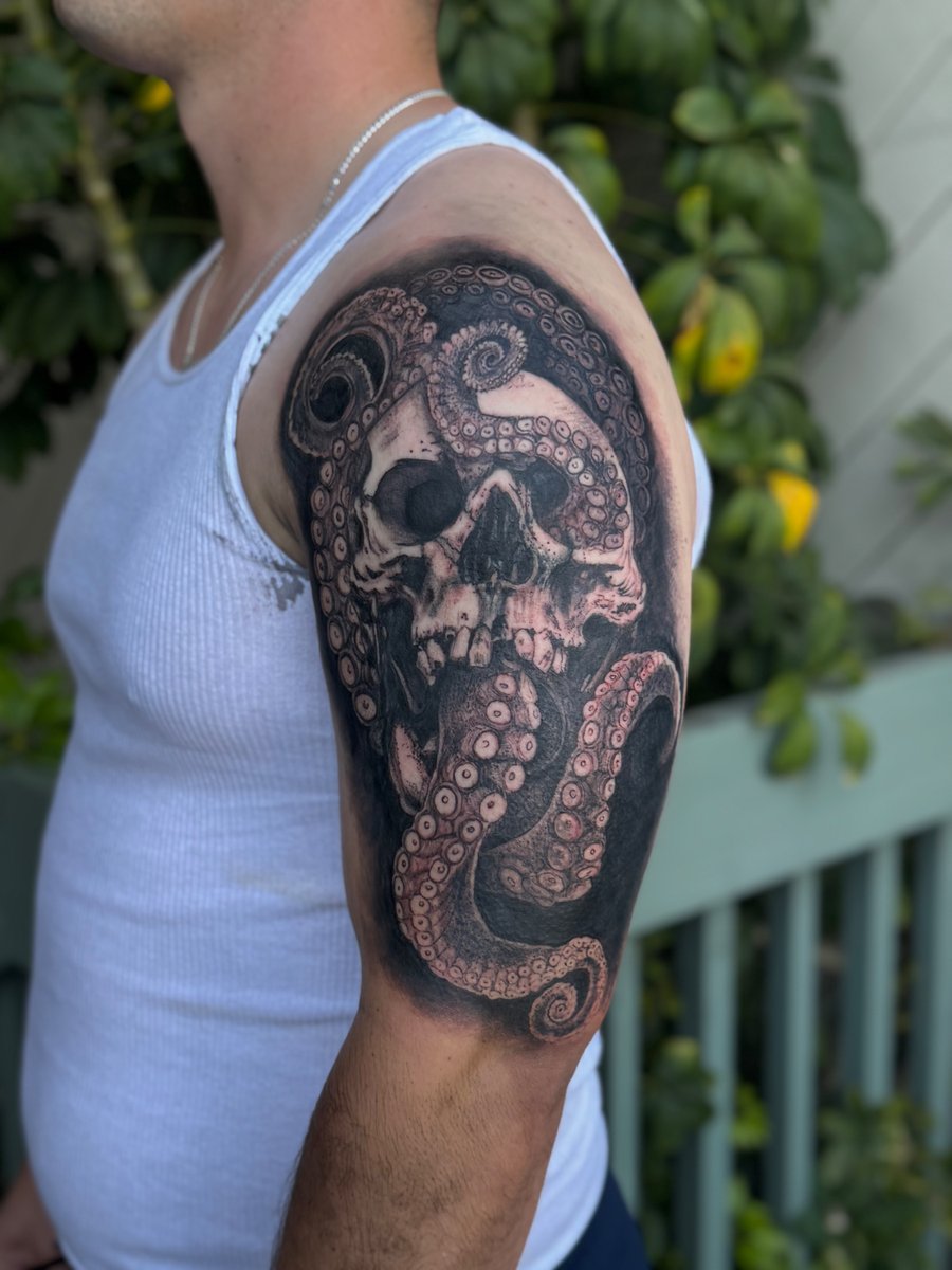 A black and grey tattoo of a skull intertwined with octopus tentacles on the upper arm, featuring realistic shading and detail — by Sandra Price, los angeles