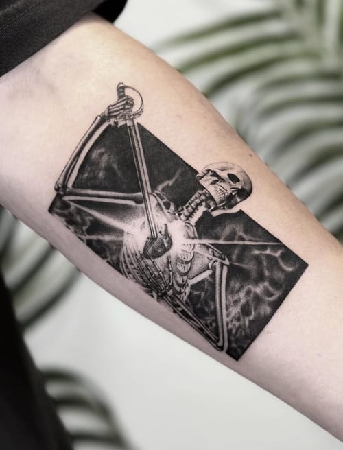 A black and grey illustrative tattoo of a skeleton holding a sword on the inner arm, featuring bold lines and high contrast — by Jian Liang, los angeles