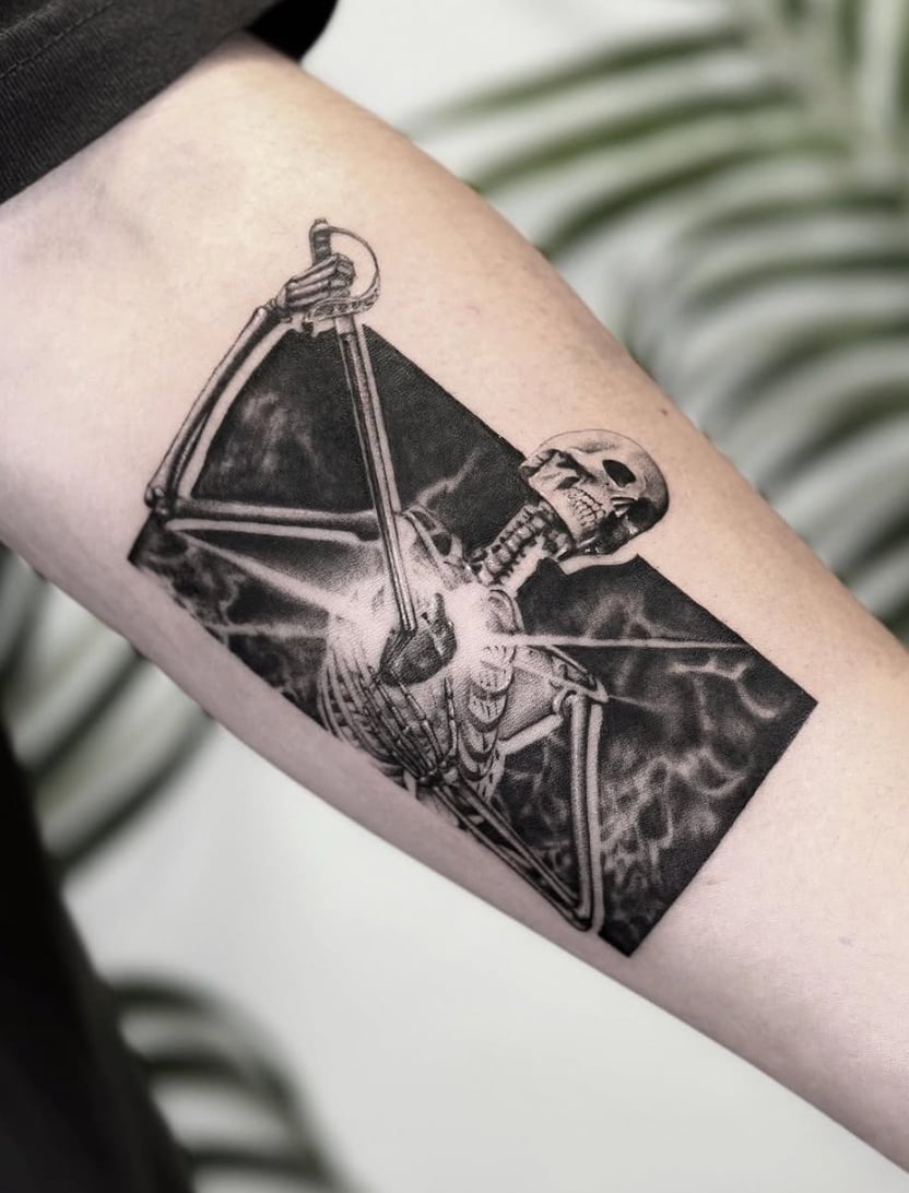 A black and grey illustrative tattoo of a skeleton holding a sword on the inner arm, featuring bold lines and high contrast — by Jian Liang, los angeles
