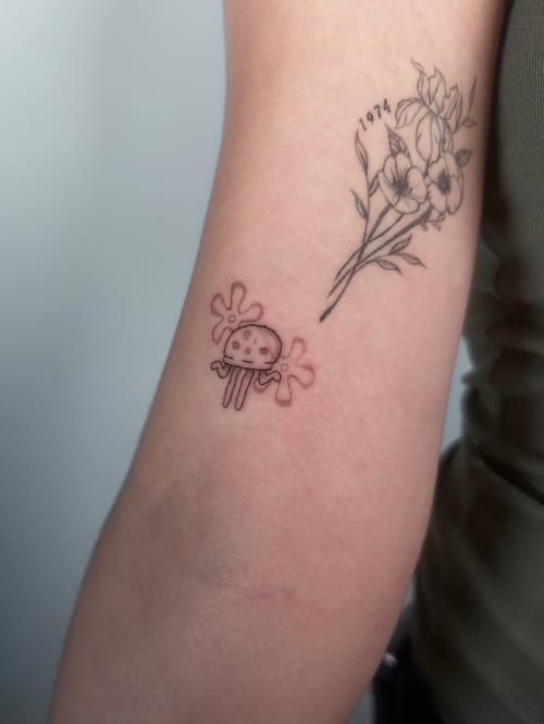 A minimalist black and grey tattoo featuring a whimsical mushroom and delicate flowers on the arm — by Brian Kies, los angeles