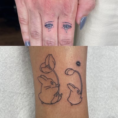 A delicate fine line tattoo featuring eyes on fingers and whimsical rabbits with flowers on the hand — by Sandra Price, los angeles