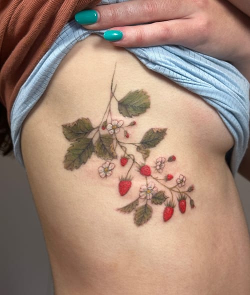 A delicate color tattoo of a strawberry plant with flowers on the rib, featuring fine line botanical details — by Melanie Benoit, los angeles