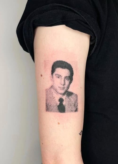 A black and grey dotwork portrait tattoo on the upper arm, featuring a stylized depiction of a person using halftone shading — by Level tattoo, los angeles