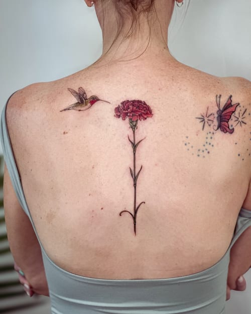 A delicate color tattoo of a hummingbird and flower on the back, featuring fine line and realistic details — by Melanie Benoit, los angeles