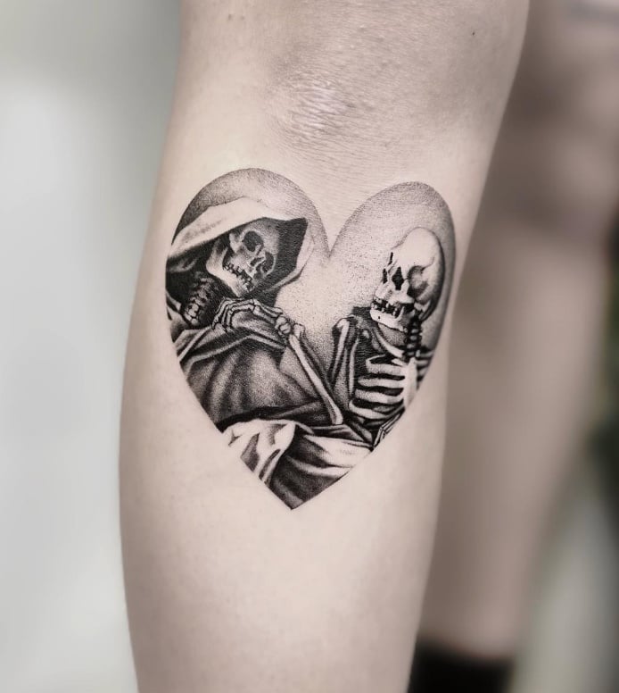 A black and grey tattoo of two skeletons inside a heart shape on the calf, featuring realistic shading and detail — by Jian Liang, los angeles
