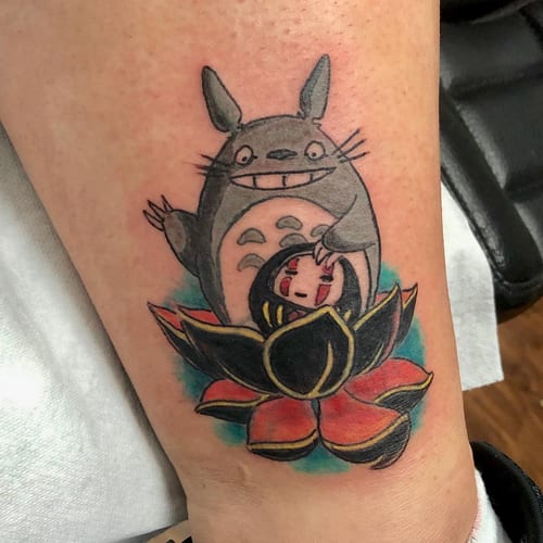 A colorful tattoo featuring Totoro and No-Face with a lotus flower on the leg, showcasing a whimsical anime style — by Sandra Price, los angeles