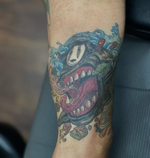 A colorful illustrative tattoo of a cartoon character with an open mouth on the forearm, featuring anime influences — by Sandra Price, los angeles