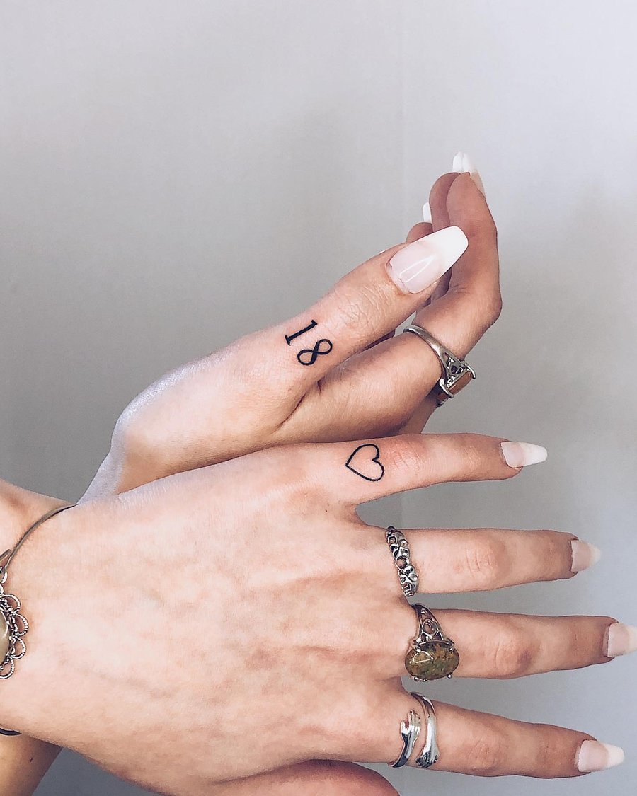 A minimalist black and grey tattoo featuring the number 18 and a heart outline on the fingers — by Level tattoo, los angeles