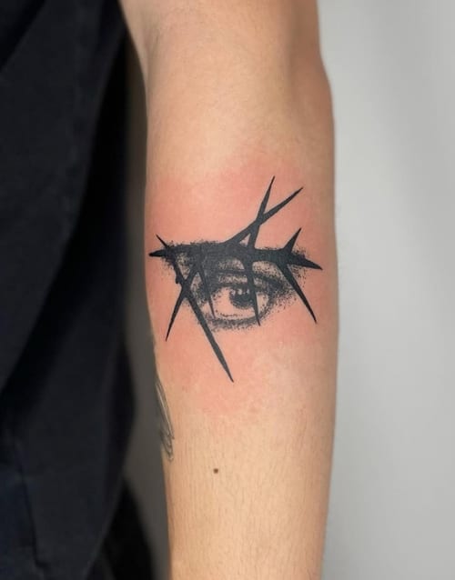 A black and grey abstract tattoo of an eye with sharp geometric elements on the arm — by Level tattoo, los angeles