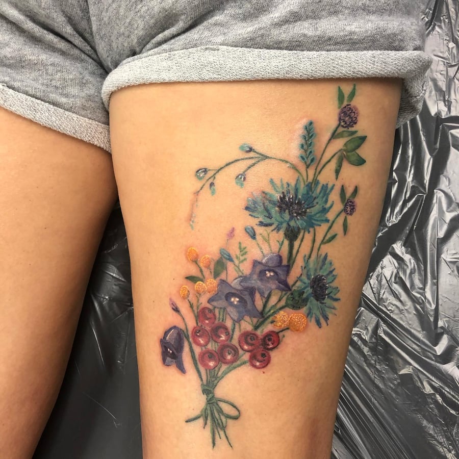 A colorful watercolor bouquet of flowers tattooed on the thigh, featuring delicate and romantic floral elements — by Sandra Price, los angeles