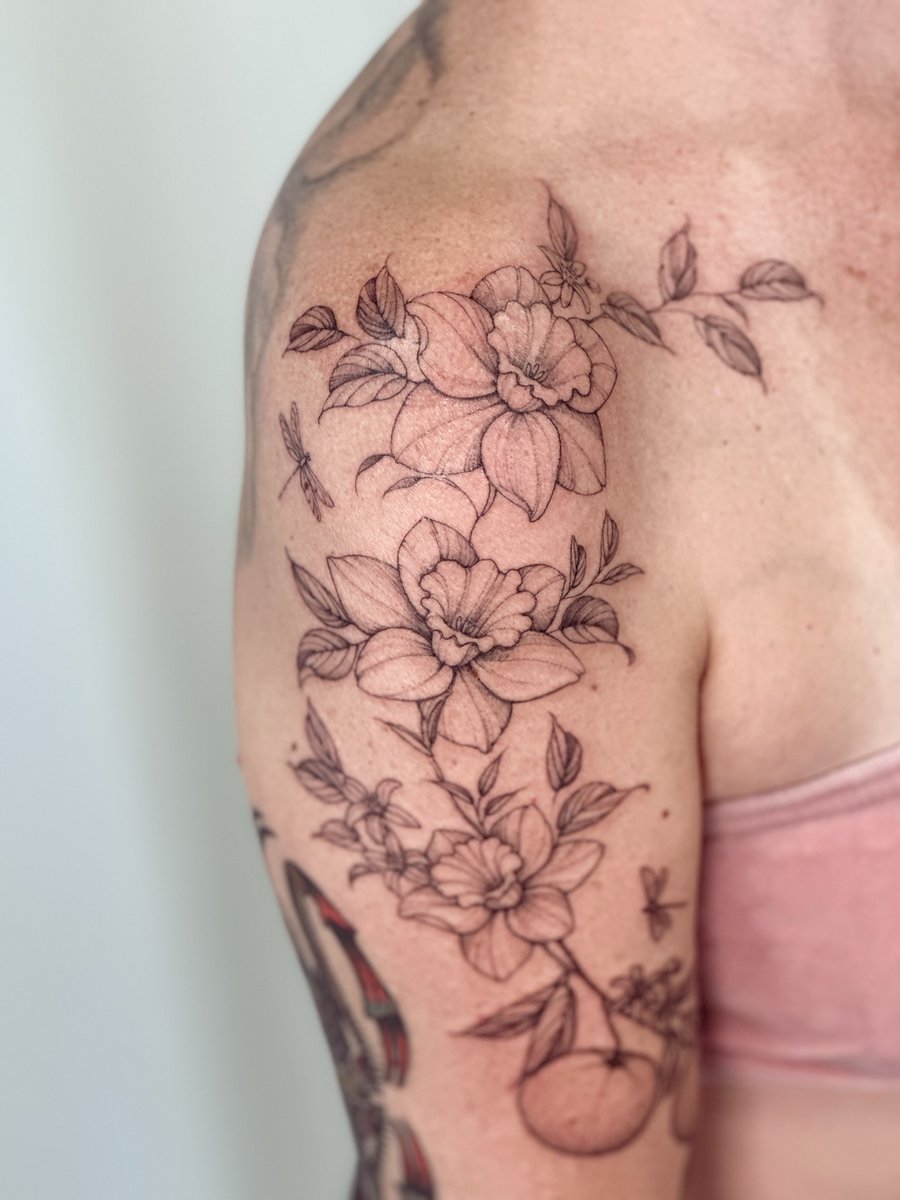 A delicate black and grey floral arrangement with dragonflies on the upper arm, featuring fine line work and a romantic feel — by Melanie Benoit, los angeles