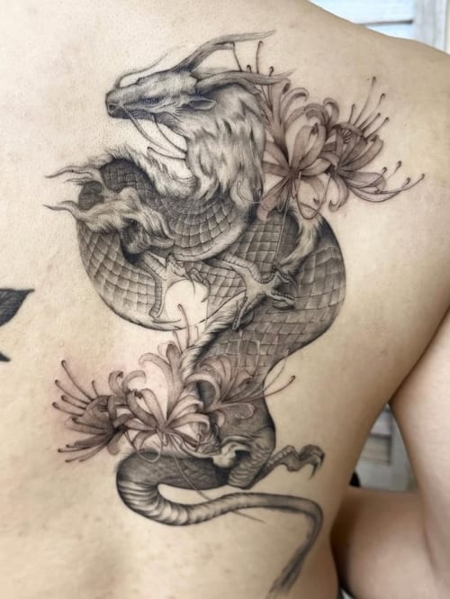 A black and grey Japanese-style dragon intertwined with flowers on the back, featuring intricate scales and detailed shading — by otaybeatdown, los angeles