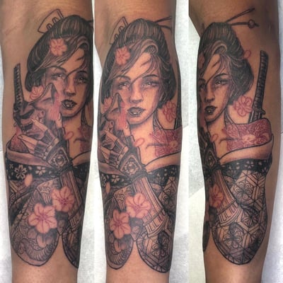 A detailed black and grey tattoo of a geisha holding a katana on the forearm, featuring intricate floral patterns and subtle color accents — by Sandra Price, los angeles