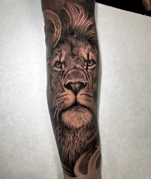 A detailed black and grey realism tattoo of a lion's face on the forearm, showcasing intricate shading and texture — by imindisoul, los angeles