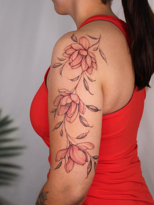 A delicate floral tattoo on the upper arm featuring fine line flowers with a subtle color palette — by Melanie Benoit, los angeles
