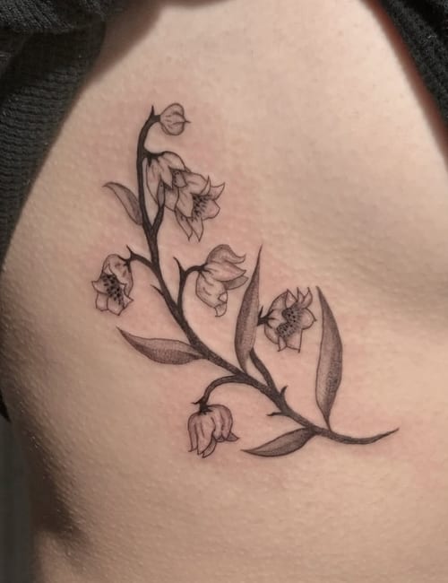 A delicate black and grey fine line floral tattoo on the rib, featuring detailed flowers and leaves — by Shelby Bianco, los angeles