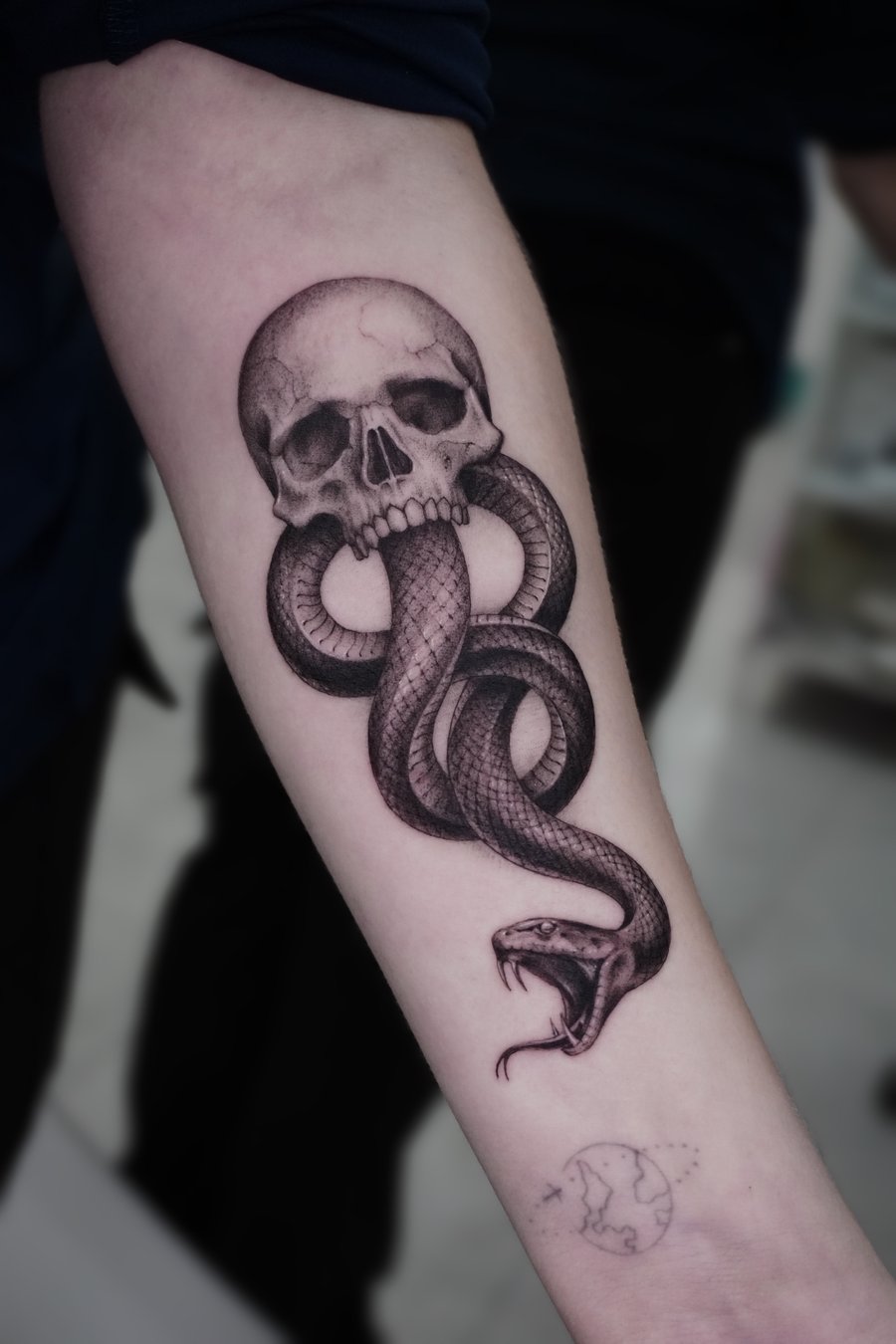 A realistic black and grey tattoo of a skull with a snake coiled through it on the forearm, featuring detailed shading and texture — by Jian Liang, los angeles