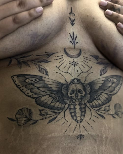 A fine line black and grey tattoo of a moth with a skull on the chest, featuring floral elements and a crescent moon — by Maddie Ramirez, los angeles