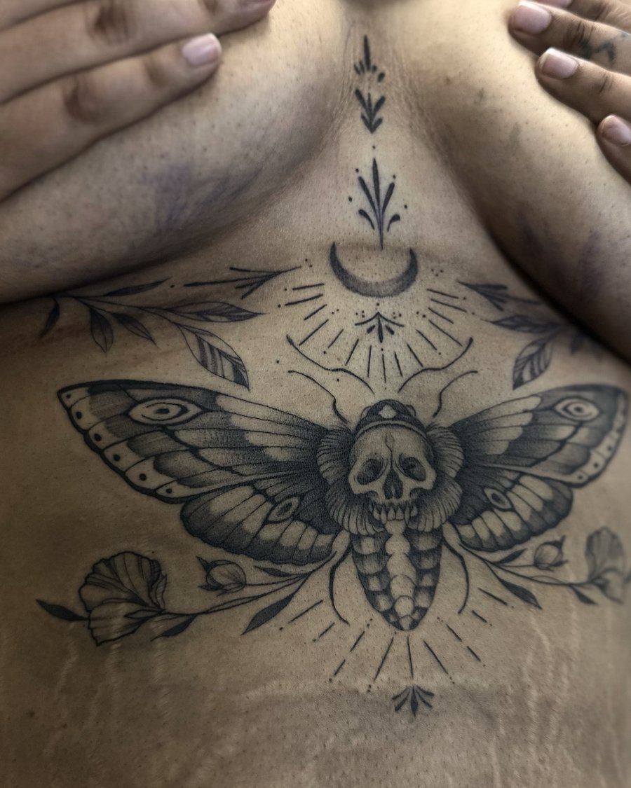 A fine line black and grey tattoo of a moth with a skull on the chest, featuring floral elements and a crescent moon — by Maddie Ramirez, los angeles