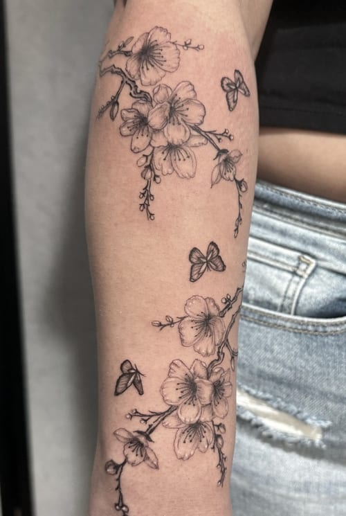 A delicate black and grey fine line tattoo of flowers and butterflies on the forearm, featuring intricate linework and shading — by Shelby Bianco, los angeles