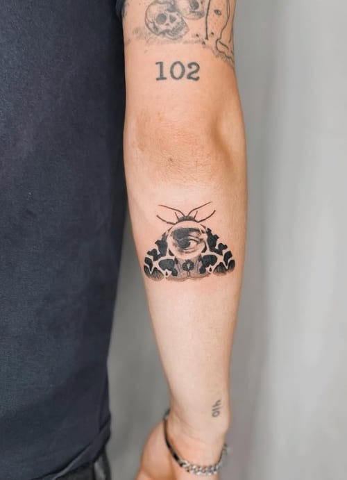 A minimalist blackwork tattoo on the forearm featuring an eye above a stylized landscape with trees and mountains — by Level tattoo, los angeles