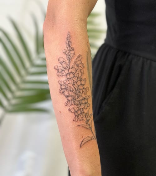 A delicate black and grey fine line flower bouquet tattoo on the forearm, featuring detailed botanical elements — by Melanie Benoit, los angeles