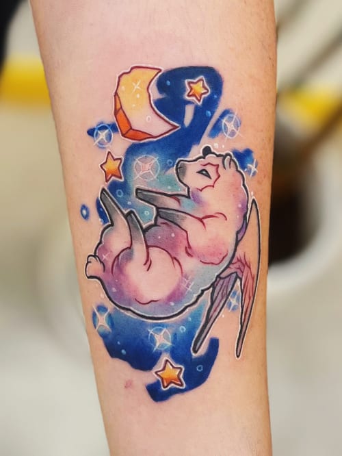 A colorful watercolor tattoo of a winged animal floating among stars and a crescent moon on the forearm, featuring vibrant blues, pinks, and oranges — by Tweetwee, los angeles