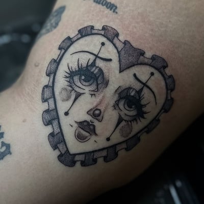 A black and grey sad clown face tattoo with fine line details and a heart shape — by Maddie Ramirez, los angeles