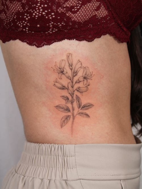 A delicate black and grey fine line flower tattoo on the rib, showcasing a botanical style — by Melanie Benoit, los angeles