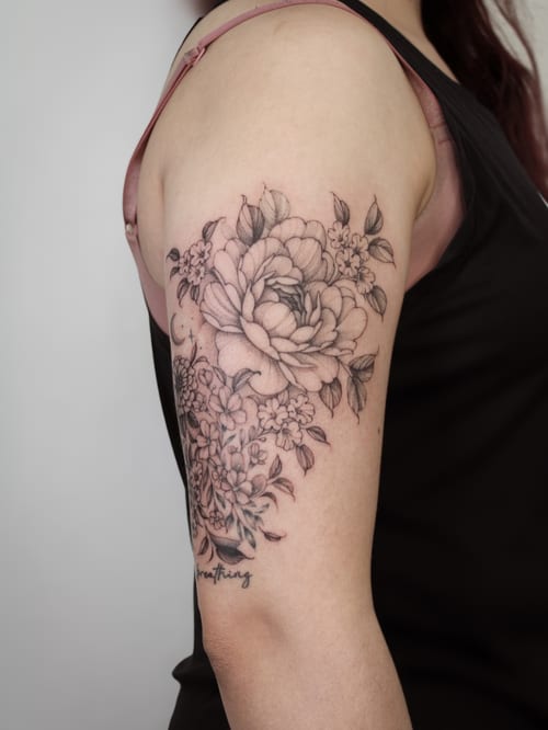A delicate black and grey floral bouquet tattoo on the upper arm with fine line details and script lettering — by Melanie Benoit, los angeles