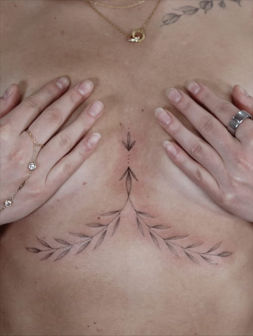 A delicate black and grey fine line tattoo of leaf branches on the chest, featuring a minimalist design — by Melanie Benoit, los angeles