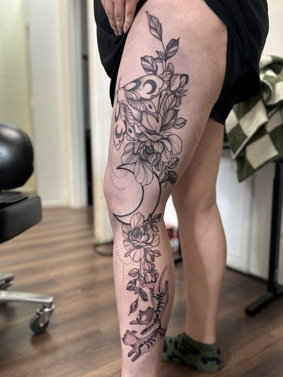 A delicate black and grey moth and floral design with a crescent moon on the thigh, featuring fine line and dotwork details — by Maddie Ramirez, los angeles