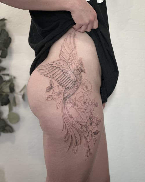 A delicate black and grey fine line tattoo of a phoenix with flowers on the thigh, featuring ornate details and elegant linework — by Melanie Benoit, los angeles
