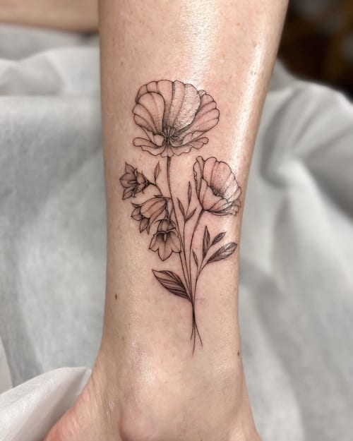 A delicate black and grey fine line flower bouquet tattoo on the ankle, featuring detailed floral elements — by Melanie Benoit, los angeles
