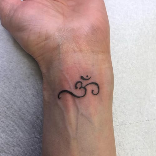 A minimalist black Om symbol tattoo on the wrist, representing spirituality and simplicity — by Sandra Price, los angeles