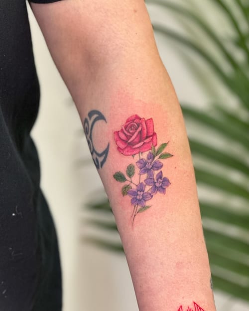 A colorful rose and floral tattoo on the forearm with fine line details and a delicate, romantic style — by Melanie Benoit, los angeles