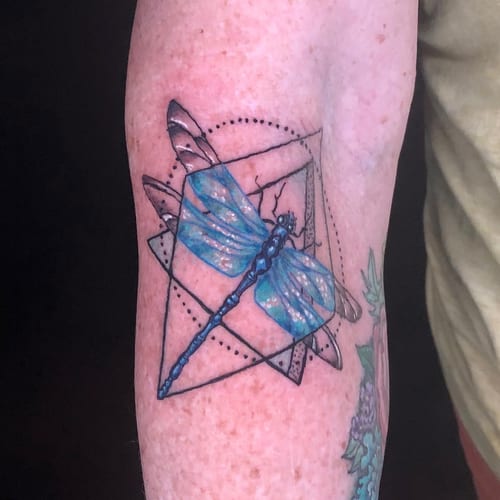 A colorful geometric dragonfly tattoo on the arm with intricate linework and blue shading — by Sandra Price, los angeles