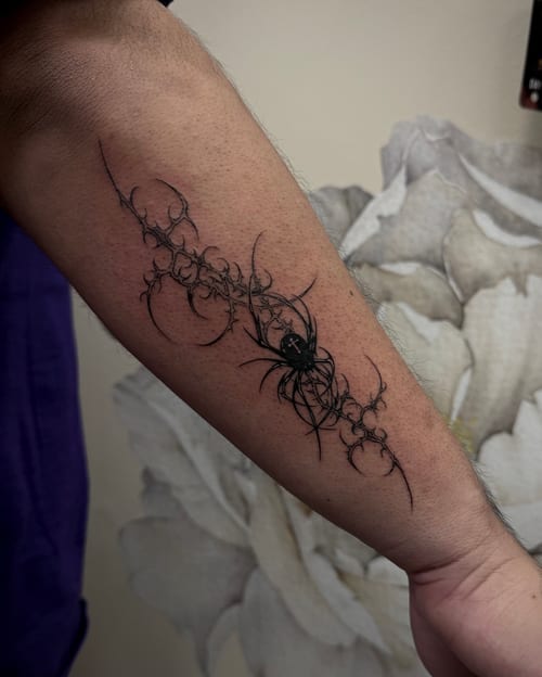 A black and grey linework tattoo of a spider on the forearm, featuring intricate web-like patterns and bold black ink — by emily, los angeles