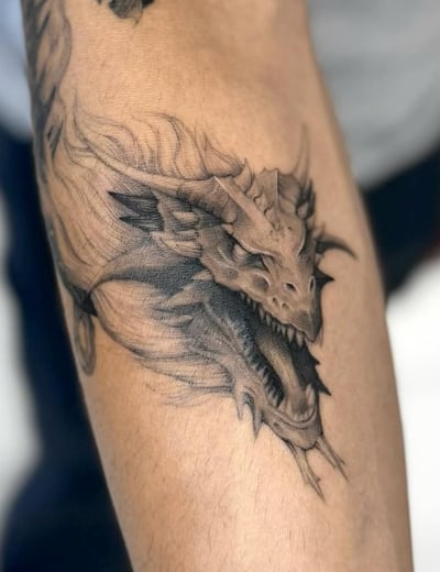 A black and grey realistic dragon head tattoo on the forearm, featuring detailed scales and fierce expression — by otaybeatdown, los angeles